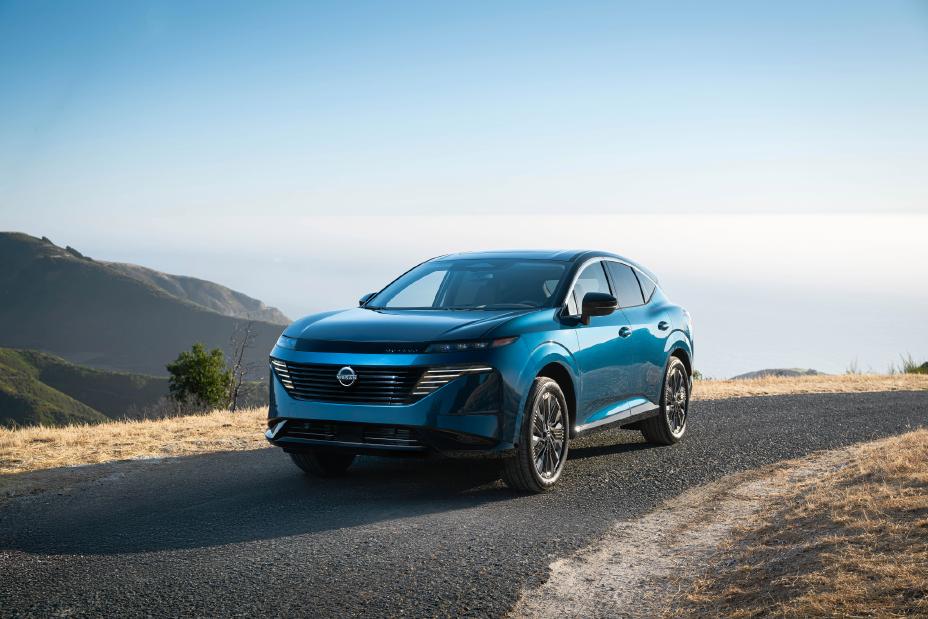 Front left 3/4 view of a blue 2025 Nissan Murano parked on a hill overlooking the ocean with other hills beside.